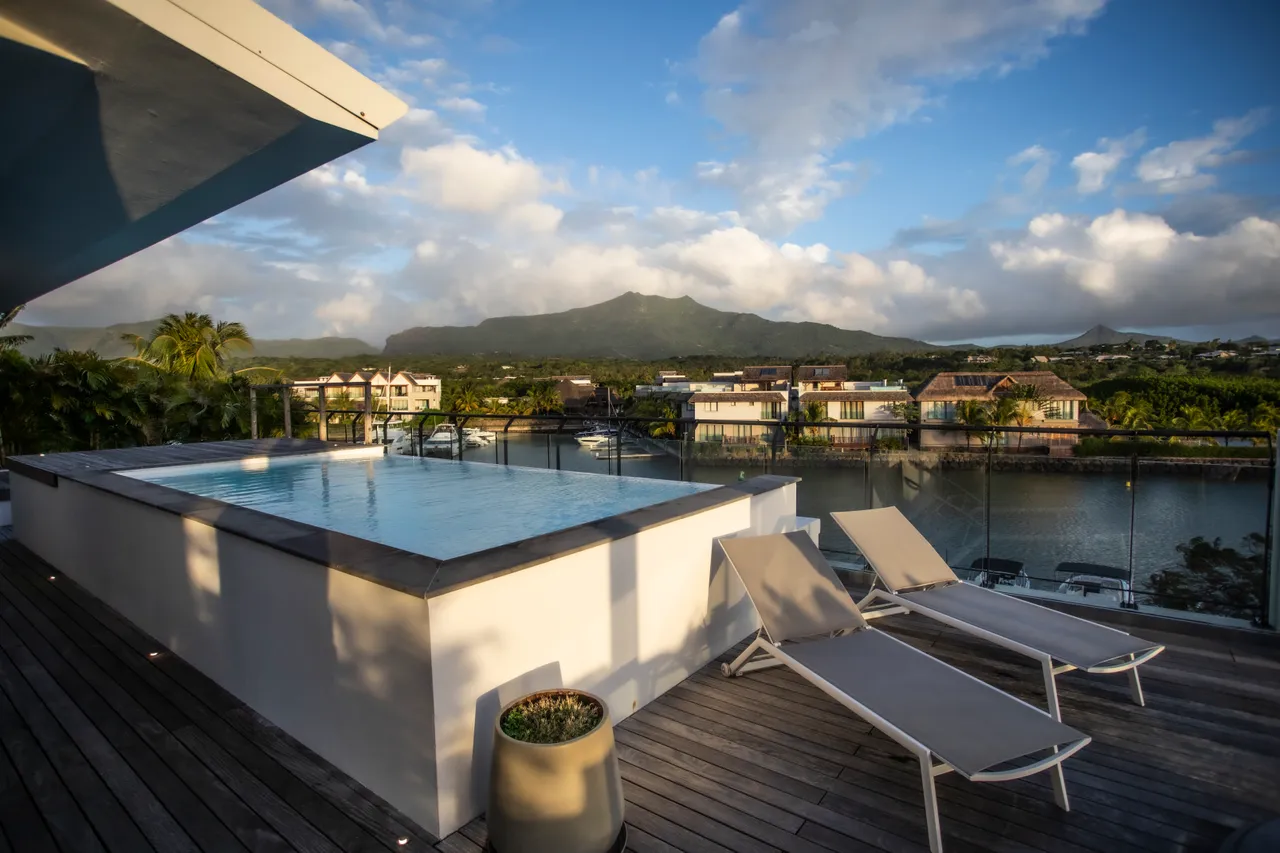 Terrasse en bois avec piscine à débordement surplombant la rivière. 

Chaises longues disposées pour profiter du soleil tout au long de la journée. 

Vue sur les montagnes créant un cadre naturel apaisant. 

Végétation environnante offrant un niveau de confidentialité à l'extérieur. 

Espace extérieur lumineux bénéficiant d'une exposition optimale au soleil.