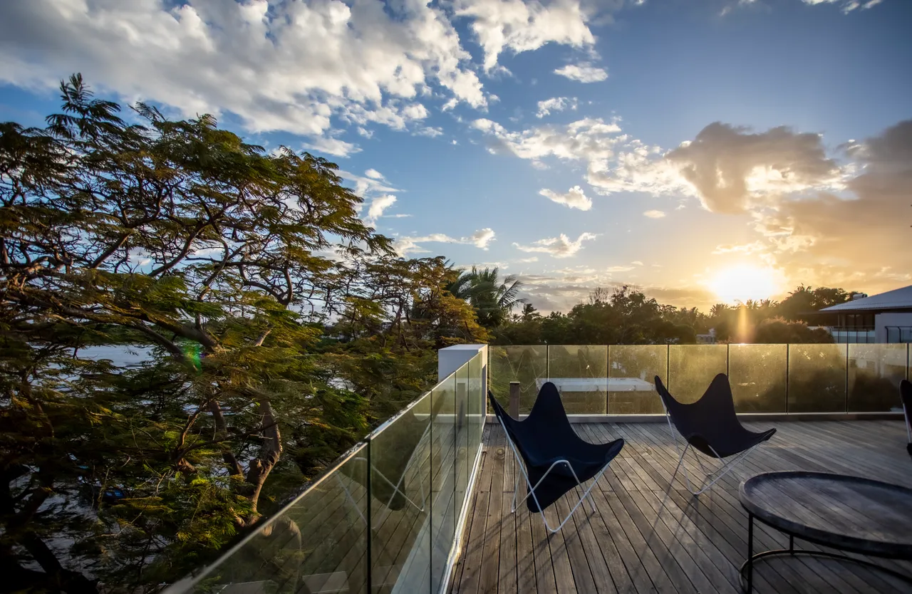 Terrasse en bois avec chaises longues contemporaines offrant une vue sur le coucher de soleil. 

Végétation environnante encadrant l'espace extérieur pour plus d'intimité. 

Lumière du soir créant une ambiance chaleureuse et apaisante. 

Espace dégagé permettant de profiter de la brise marine. 

Accès direct à la piscine depuis la terrasse pour un