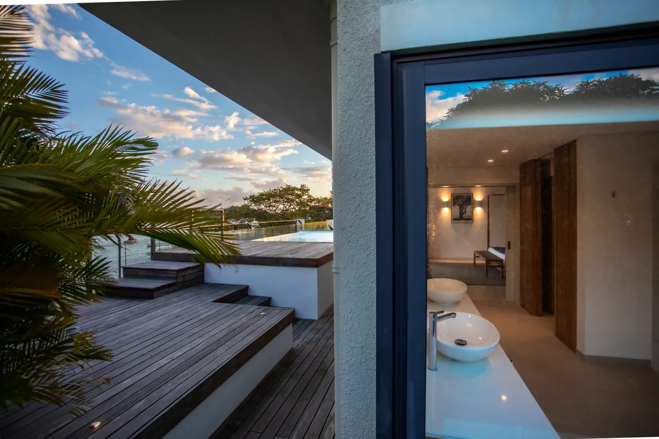 Salle de bains moderne avec double vasque élégante et éclairage intégré. 

Accès direct à la terrasse en bois depuis la salle de bains. 

Végétation environnante offrant une touche naturelle et apaisante. 

Grandes fenêtres permettant une luminosité optimale dans l'espace. 

Espace bien agencé favorisant confort et fonctionnalité.