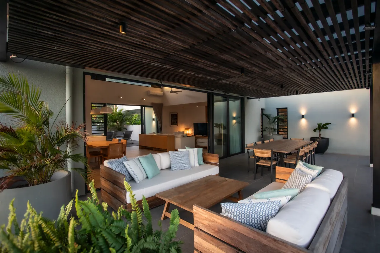 Espace de vie extérieur avec mobilier en bois offrant confort et convivialité. 

Plantes vertes ajoutant une touche naturelle à l'environnement. 

Lumière naturelle filtrée par le plafond en lattes, créant une ambiance agréable. 

Coin repas intégré pour des repas en plein air. 

Accès direct à l'intérieur facilitant la circulation entre les espaces.