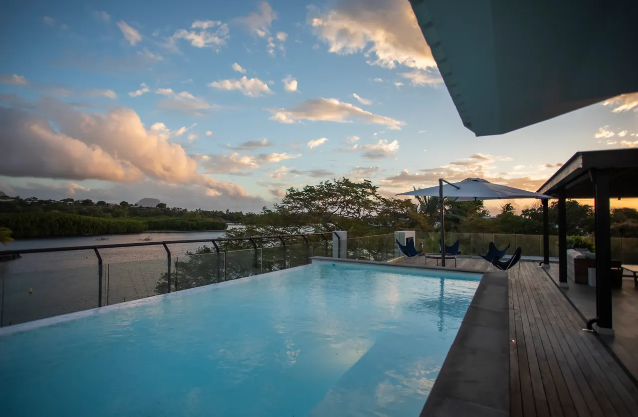 Espace extérieur avec piscine et chaises longues.  

Terrasse en bois offrant une vue sur la nature environnante.  

Auvent blanc protégeant la zone de détente.  

Végétation luxuriant ajoutant une touche naturelle au décor.  

Ambiance tranquille face à l'eau au crépuscule.