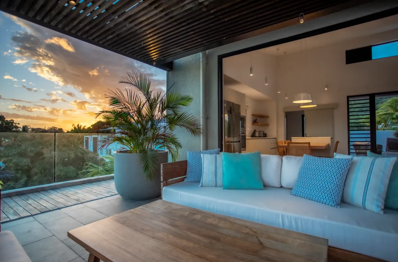 Teintes neutres et bois créent une atmosphère apaisante. Espace salon avec canapé et vue sur la nature. Lumières suspendues ajoutent une touche moderne à l'intérieur. Coin repas en bois avec vue dégagée sur l'extérieur. Plantes vertes apportent une touche de fraîcheur à l'espace. Grandes baies vitrées offrant une luminosité naturelle. Terrasse spacie