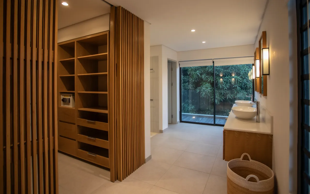 Sol en carrelage clair avec rangements intégrés en bois pour un agencement pratique. 

Espace lumineux grâce à une grande baie vitrée donnant sur le jardin. 

Doubles vasques sur un plan de travail épuré, offrant fonctionnalité et style. 

Éclairage doux créant une ambiance relaxante dans la salle de bains. 

Accès direct au jardin depuis cet espace,