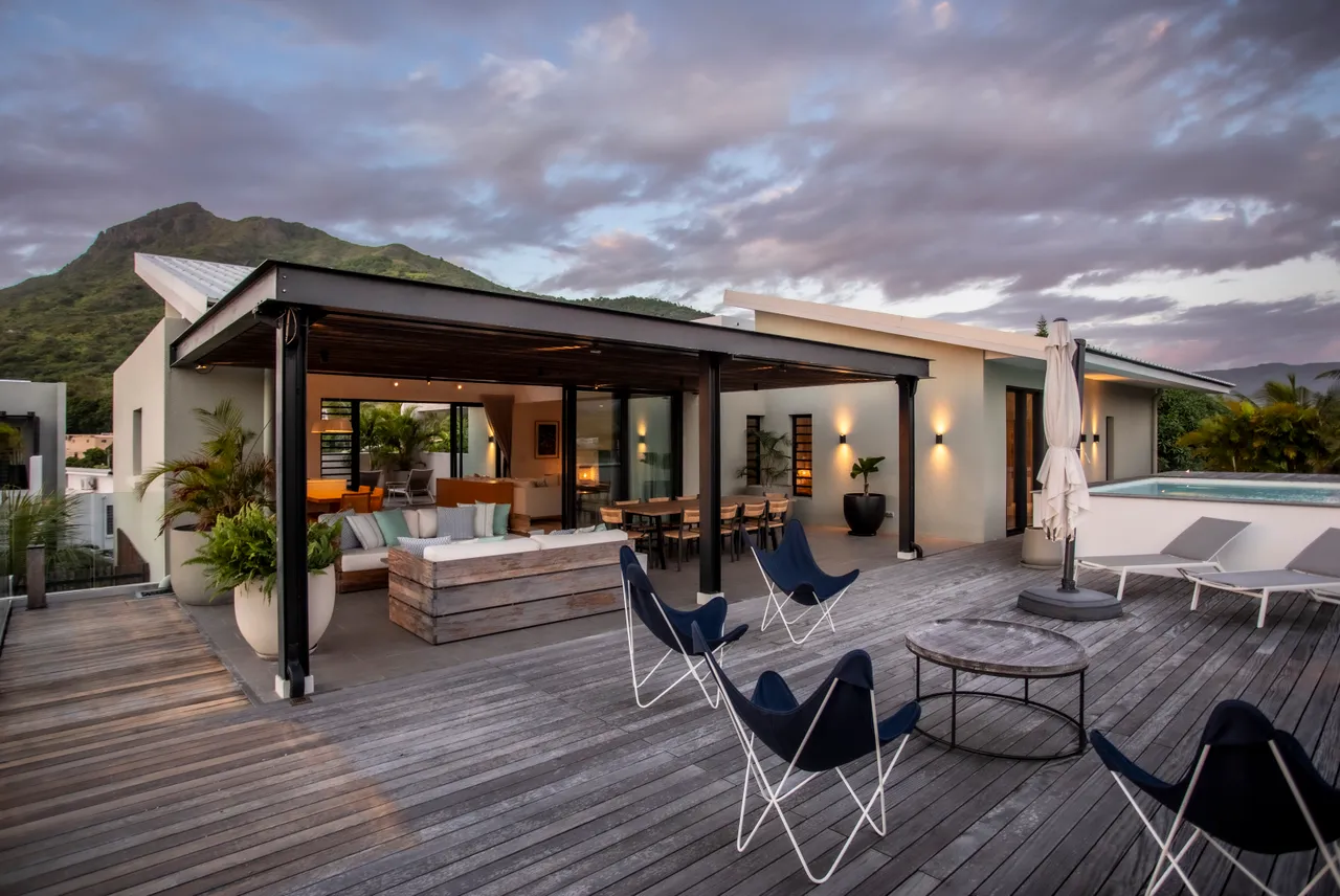 Espace extérieur spacieux avec salon lounge et vue sur les montagnes. 

Mobilier moderne installé sur une terrasse en bois pour les moments de détente. 

Parasol déployé pour créer de l'ombre lors des journées ensoleillées. 

Accès direct à la piscine depuis la terrasse pour un rafraîchissement immédiat. 

Éclairage intégré offrant une ambiance agréable en soirée.