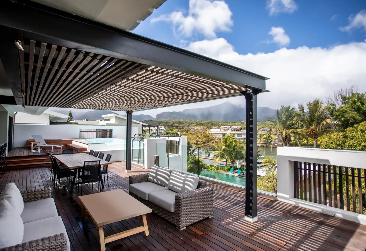 Terrasse spacieuse avec mobilier en bois et vue dégagée sur les environs.  
Zone ombragée idéale pour des repas en extérieur et moments de détente.  
Espace de vie extérieur élégant avec un agencement fonctionnel pour les loisirs.  
Piscine privée visible depuis la terrasse, créant un lien avec l'extérieur.