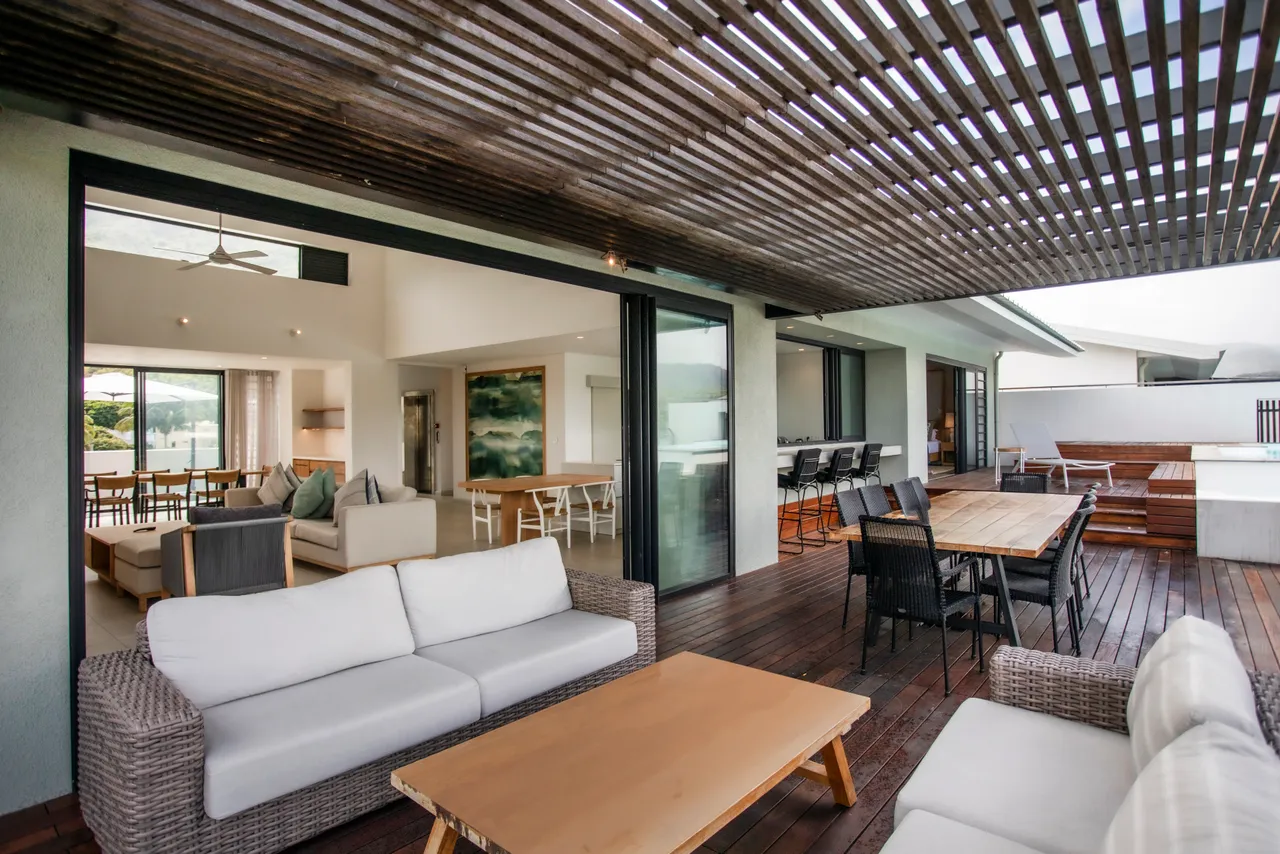 Terrasse en bois avec mobilier confortable et vue dégagée sur l'environnement.  
Espace ombragé parfait pour des repas en plein air et moments de détente.  
Piscine privée à proximité, intégrant l'espace extérieur de manière harmonieuse.  
Agencement fonctionnel favorisant le confort pour profiter des loisirs en extérieur.  
Ouvertures sur l'intérieur permettant une circulation fluide entre les