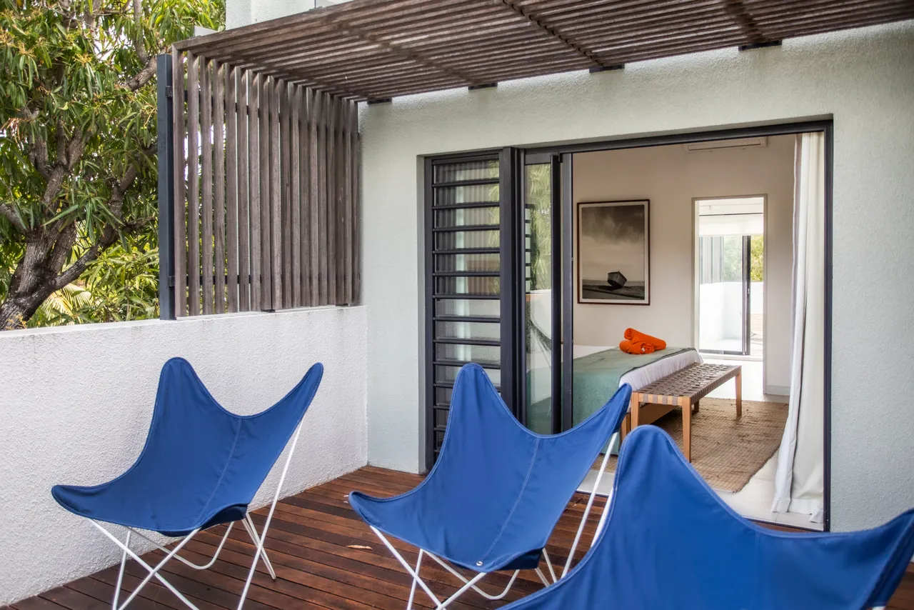 Terrasse en bois avec chaises confortables offrant une vue sur l'extérieur.  
Accès direct à la chambre à travers des portes coulissantes.  
Espace extérieur aménagé pour la détente et le repos.  
Ouverture sur l'intérieur créant une fluidité entre les espaces.  
Zone ombragée propice à des moments agréables en plein air.
