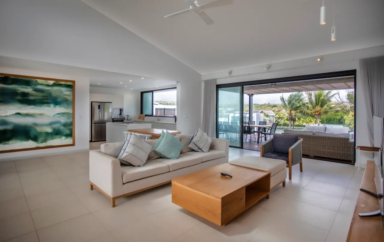 Lumière naturelle inondant le salon grâce aux grandes baies vitrées.  
Espace ouvert comprenant un coin salon et une cuisine intégrée.  
Mobilier en bois clair ajoutant une touche de chaleur à l'intérieur.  
Plafond haut renforçant la sensation d'espace et de confort.  
Accès direct à la terrasse, favorisant la continuité entre intérieur et extérieur.