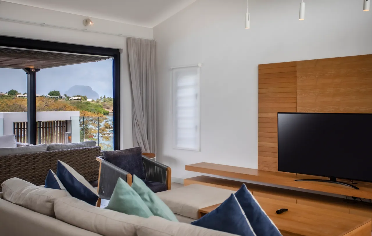 Couleurs neutres et textures douces dans l'espace de vie.  
Coin salon avec télévision intégrée et accès direct à la terrasse.  
Fenêtres généreuses offrant une vue sur la nature environnante.  
Mobilier en bois clair créant une atmosphère chaleureuse et accueillante.  
Agencement ouvert favorisant la fluidité entre les espaces intérieurs et extérieurs.