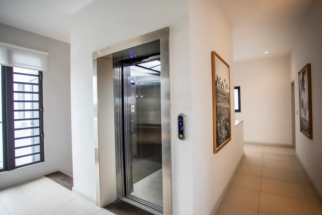 Ascenseur moderne avec accès direct au penthouse.  
Mur en blanc épuré offrant une ambiance lumineuse.  
Sols en carrelage clair renforçant la sensation d’espace.  
Éclairage intégré soulignant les œuvres d'art accrochées.  
Agencement fonctionnel facilitant la circulation dans la galerie.