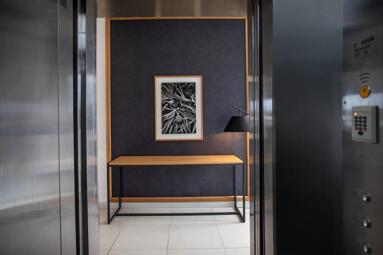 Ouverture sur l'extérieur grâce à de grandes fenêtres lumineuses.  
Mobilier minimaliste en bois offrant un espace pratique et fonctionnel.  
Éclairage intégré créant une ambiance chaleureuse dans la galerie.  
Mur texturé ajoutant un intérêt visuel à l'espace.  
Accès facile aux différentes zones grâce à l'agencement fluide.