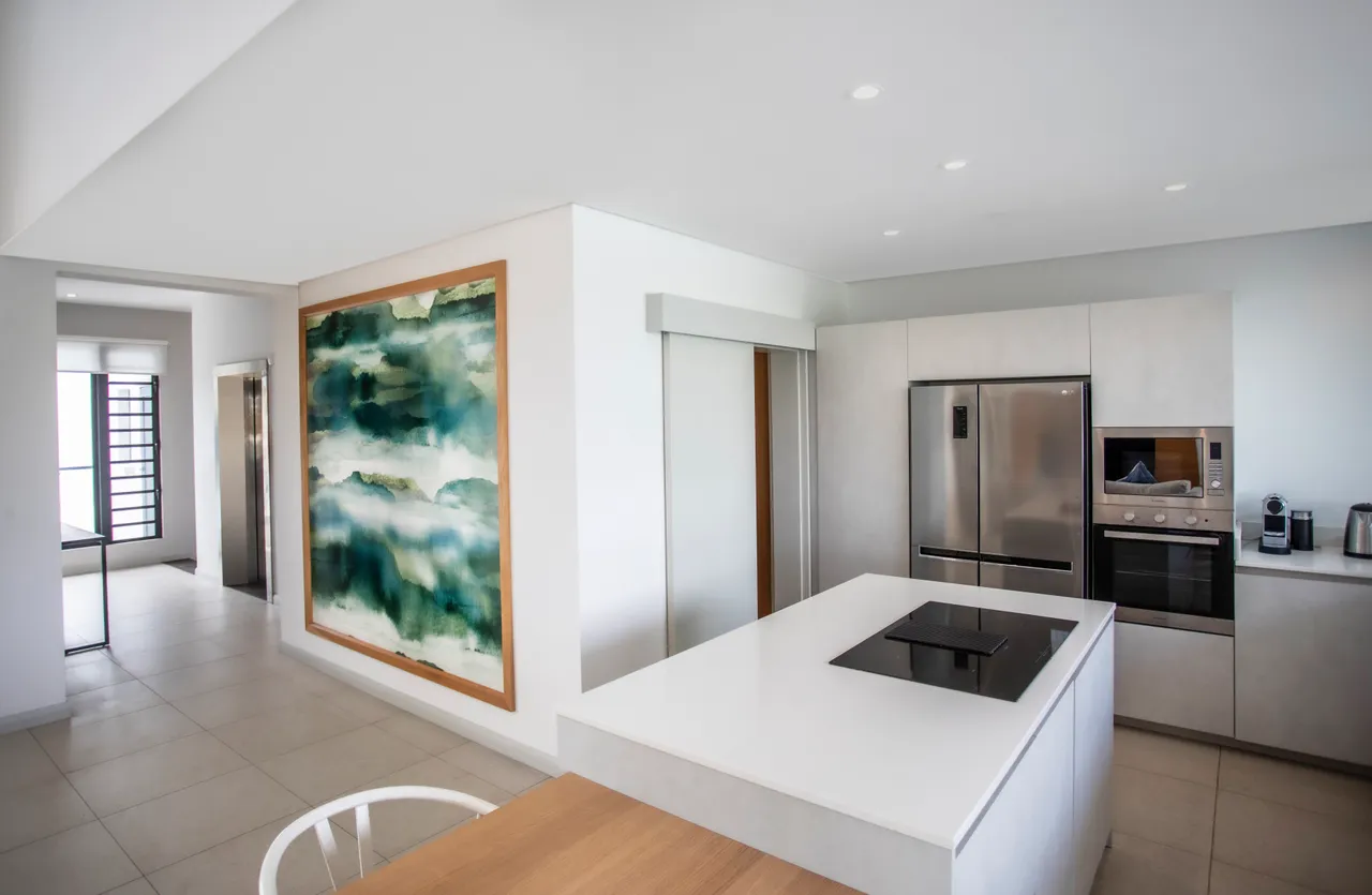 Cuisine moderne avec plan de travail en marbre et électroménagers intégrés.  
Espace ouvert permettant une interaction fluide avec le coin salle à manger.  
Éclairage doux mettant en valeur le design épuré de la pièce.  
Mur décoratif ajoutant une touche artistique à l'environnement.  
Rangement optimisé facilitant l'organisation des ustensiles et provisions.