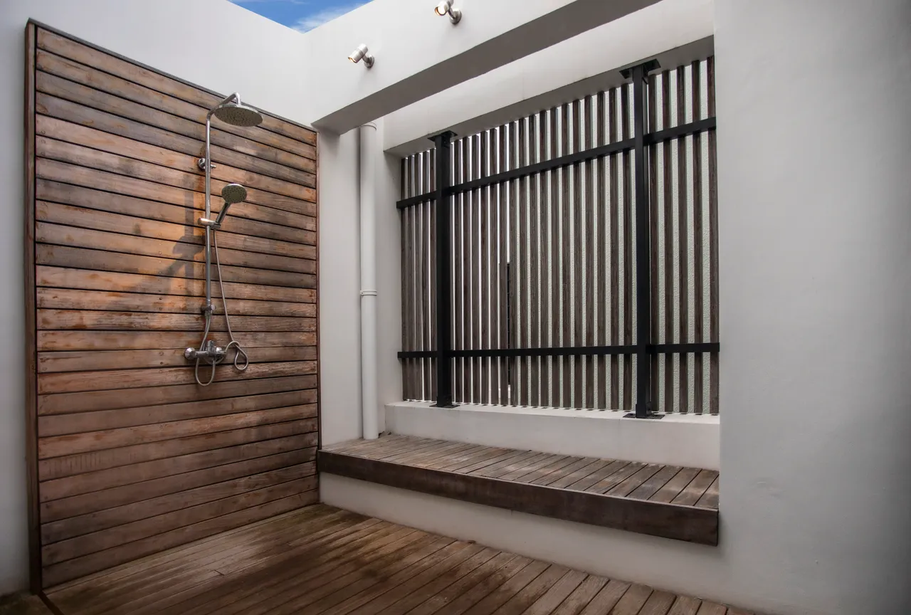 Douche extérieure avec parois en bois et espace de rangement en bois.  
Sols en bois créant une atmosphère naturelle et relaxante.  
Éclairage intégré pour une ambiance agréable lors de l'utilisation.  
Agencement pratique favorisant l'intimité tout en étant accessible.  
Détails en bois ajoutant une touche de chaleur à l'espace.