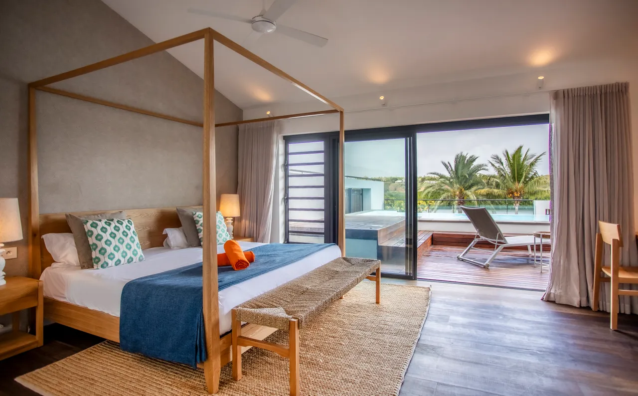 Chambre 1 avec lit à baldaquin et accès direct à la terrasse.  
Grandes fenêtres offrant une vue sur la piscine privée.  
Mobilier en bois clair ajoutant une note apaisante à l'espace.  
Tapis en jute créant une ambiance naturelle et chaleureuse.  
Espace de rangement fonctionnel pour un séjour organisé.