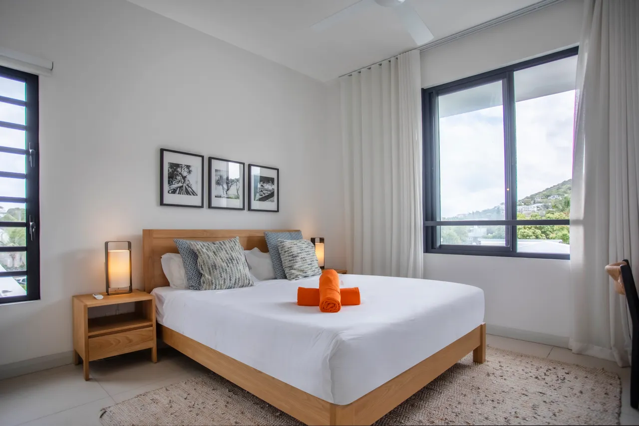 Chambre avec fenêtres panoramiques offrant une vue sur l'extérieur.  
Mobilier en bois clair ajoutant simplicité et confort à l'espace.  
Tapis en jute apportant une texture naturelle au sol.  
Éclairage doux créant une ambiance sereine dans la pièce.  
Espace de rangement intégré pour une meilleure organisation.