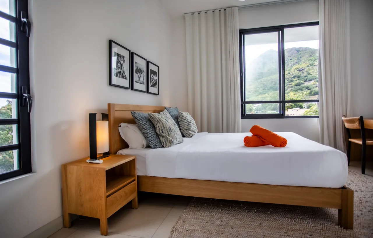 Couleurs douces et mobilier en bois clair dans la chambre.  
Fenêtres offrant une vue sur le paysage environnant.  
Tapis texturé ajoutant une touche de confort au sol.  
Lampes de chevet fournissant un éclairage doux pour la nuit.  
Espace de rangement intégré pour un séjour bien organisé.