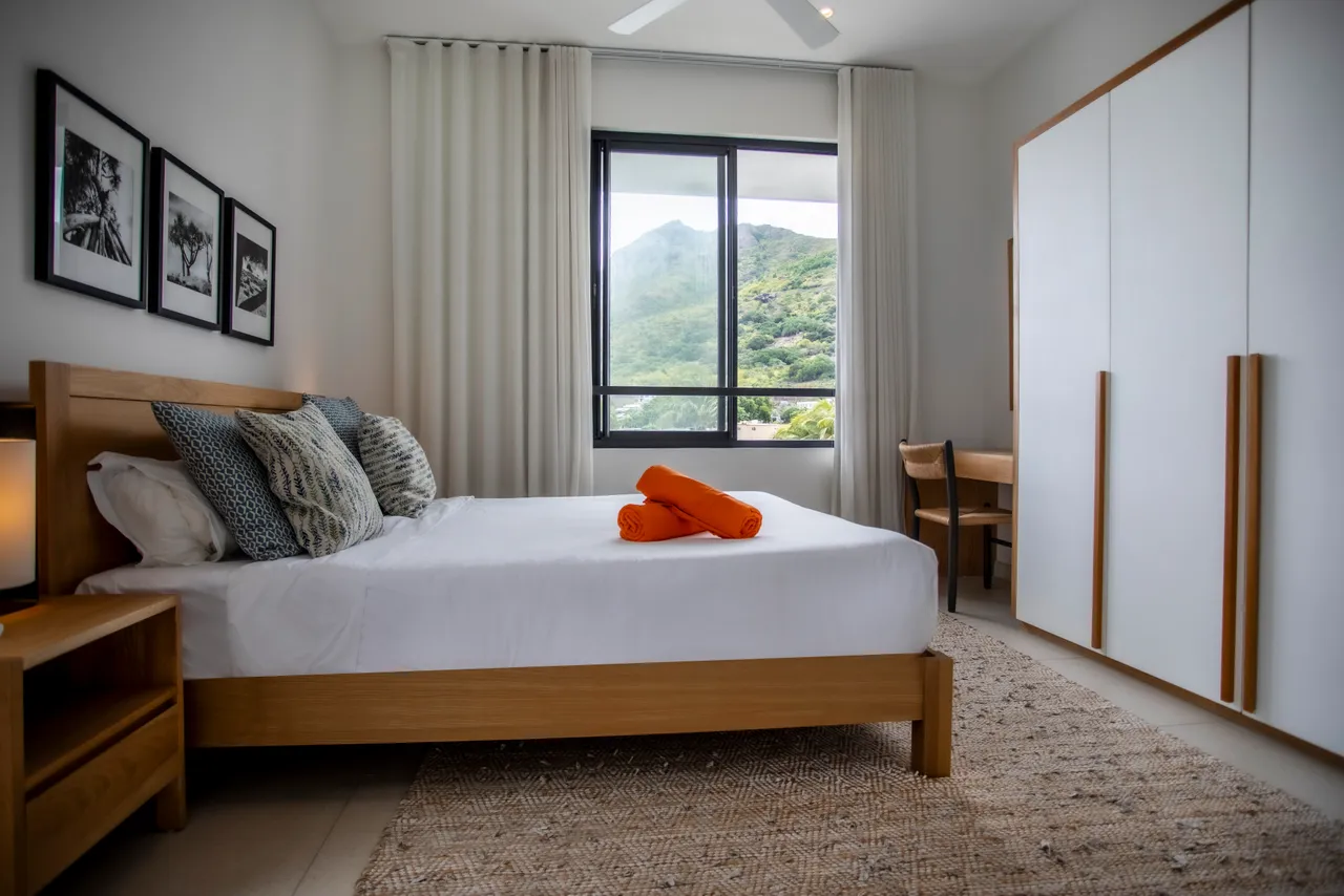 Chambre avec vue sur les montagnes et mobilier en bois clair.  
Linge de lit soigneusement disposé pour une présentation soignée.  
Tapis en jute ajoutant une texture naturelle au sol.  
Éclairage doux provenant des lampes de chevet intégrées.  
Espace de rangement pratique pour une organisation optimale.