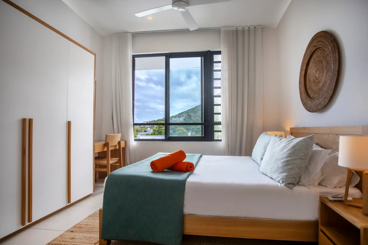 Chambre avec vue sur la montagne et mobilier en bois clair.  
Lit queen-size agrémenté de linge de lit coordonné.  
Éclairage doux provenant des lampes de chevet intégrées.  
Fenêtre large laissant entrer la lumière naturelle dans la pièce.  
Espace de rangement discret intégré pour un séjour organisé.