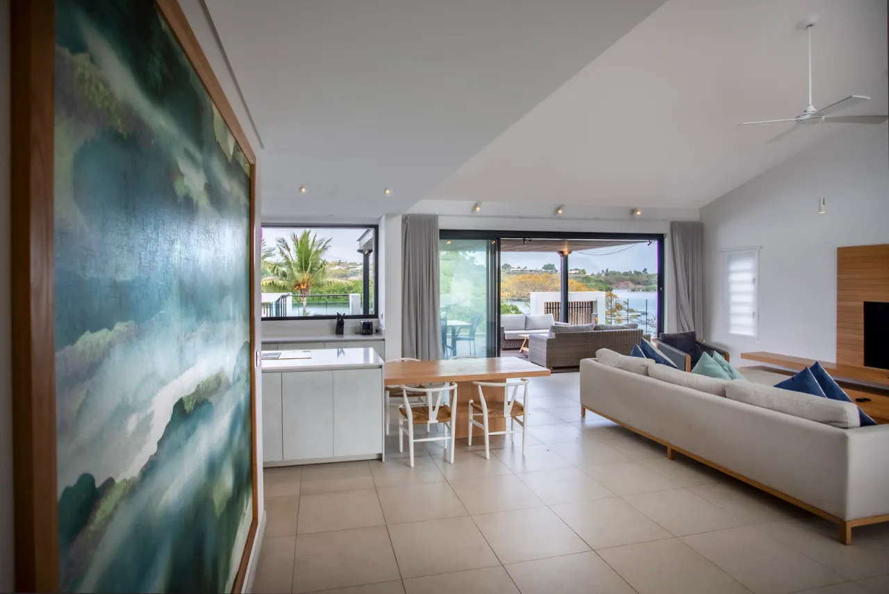 Espace de vie lumineux avec grandes fenêtres et vue sur l'extérieur.  
Mobilier contemporain incluant un canapé et une table à manger.  
Cuisine ouverte intégrée offrant un espace fonctionnel et pratique.  
Éléments décoratifs modernes ajoutant une touche artistique à la pièce.  
Terrasse accessible depuis le salon, prolongeant l'espace intérieur.