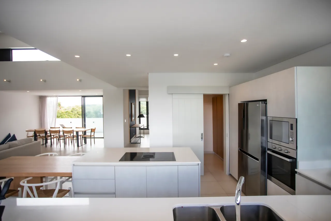 Cuisine complète avec un agencement moderne et des appareils intégrés.  
Îlot central fonctionnel offrant un espace de préparation pratique.  
Lumière naturelle inondant la pièce grâce aux grandes fenêtres.  
Mobilier épuré et contemporain pour un environnement accueillant.  
Accès direct à la terrasse depuis la cuisine, facilitant la circulation.