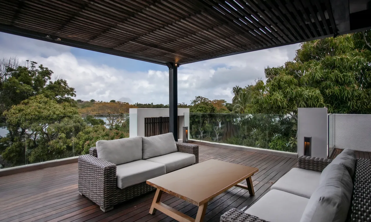 Terrasse en bois équipée d'un salon de jardin pour le confort extérieur.  
Végétation environnante créant un cadre naturel et apaisant.  
Plafond en bois ajouré apportant une touche d'élégance à l'espace.  
Vue dégagée sur le paysage environnant depuis la terrasse.  
Éclairage discret intégrant des appliques murales pour les soirées.