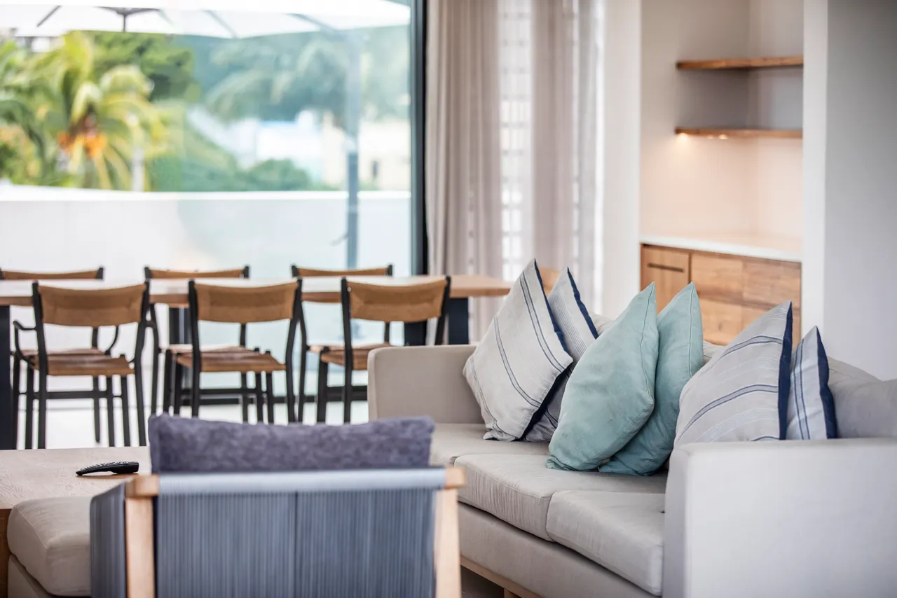 Tons neutres avec coussins décoratifs apportant une touche de confort.  
Espace de vie ouvert avec accès à la terrasse et vue dégagée.  
Mobilier contemporain incluant un canapé et une table basse.  
Coin repas qui relie le salon à la cuisine, facilitant les interactions.  
Lumière naturelle inondant la pièce grâce aux grandes baies vitrées.