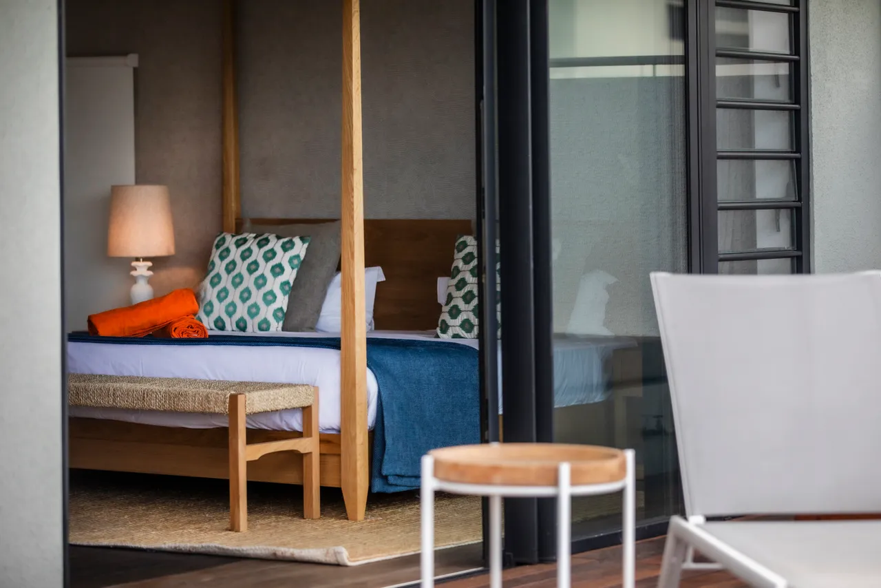 Tons neutres avec des éléments en bois créant une atmosphère apaisante.  
Lit king-size avec linge de lit de qualité pour un confort optimal.  
Accès direct à la terrasse depuis la chambre, élargissant l'espace.  
Luminaires contemporains ajoutent une touche moderne à l'intérieur.  
Grande fenêtre offrant une vue dégagée sur l'extérieur.