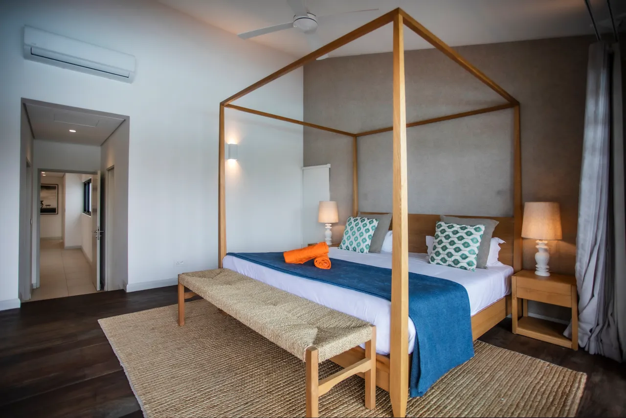 Tons doux avec un lit king-size et des coussins décoratifs.  
Chevet en bois clair avec lampes offrant une lumière apaisante.  
Espace de rangement intégré pour une organisation pratique.  
Texture du tapis apportant une touche chaleureuse à la chambre.  
Accès direct à la salle de bain depuis la chambre pour plus de commodité.
