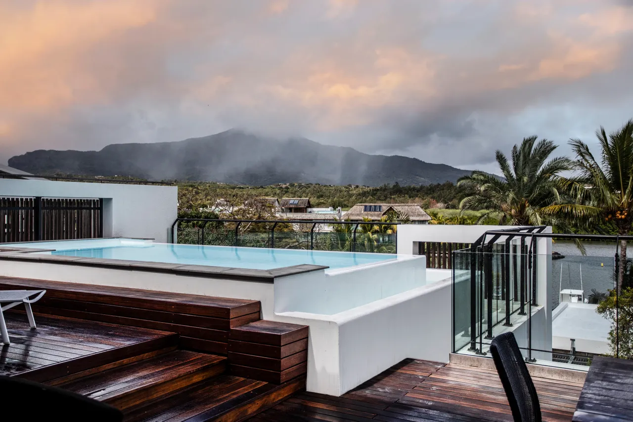 Espace extérieur avec piscine à débordement offrant une vue sur les montagnes.  
Terrasse boisée équipée de chaises pour profiter du coucher de soleil.  
Végétation environnante apportant une touche naturelle à l'ambiance.  
Zone de repas extérieure avec une table pour des moments conviviaux.  
Luminosité naturelle accentuée par la disposition ouverte de l'espace.