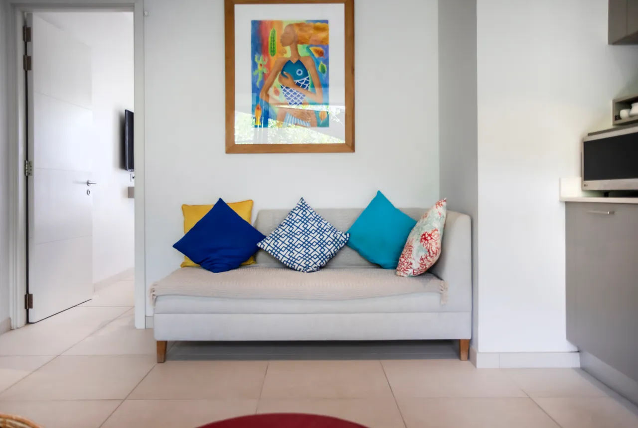 Coussins colorés sur un canapé offrant une touche de confort.  
Table basse en bois clair ajoutant une note naturelle à l'espace.  
Cuisine moderne avec des appareils intégrés et un comptoir fonctionnel.  
Éclairage naturel inondant le coin salon par de grandes fenêtres.  
Décoration murale artistique contribuant à l'ambiance intérieure.  
Accès direct à la salle