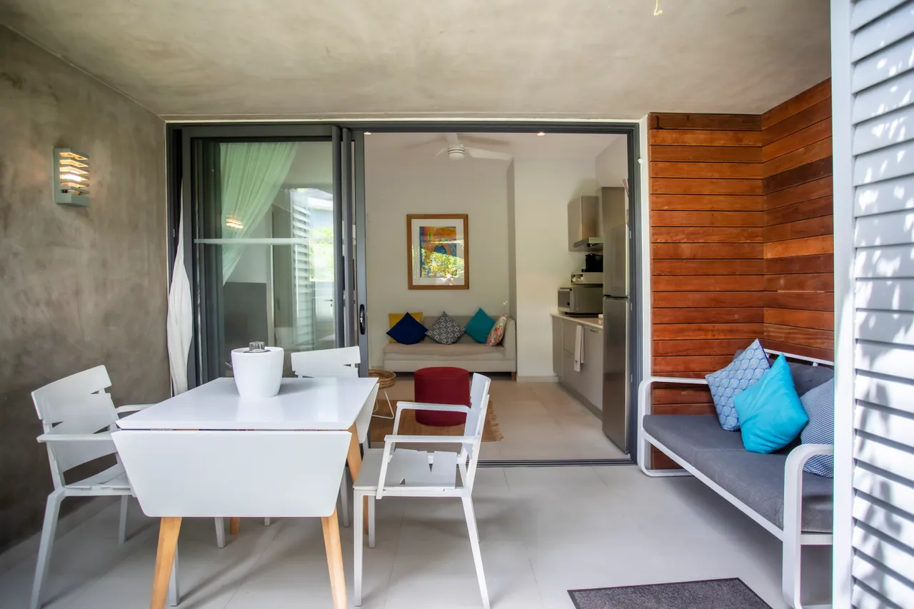 Terrasse spacieuse avec mobilier extérieur et coin repas.  
Vue dégagée depuis la salle à manger lumineuse.  
Zone de détente avec canapé et coussins colorés.  
Ouverture sur l'intérieur renforçant la connexion entre les espaces.  
Détails en bois ajoutant une texture chaleureuse à l'environnement.  
Éclairage naturel inondant l'espace grâce aux grandes baies vitr