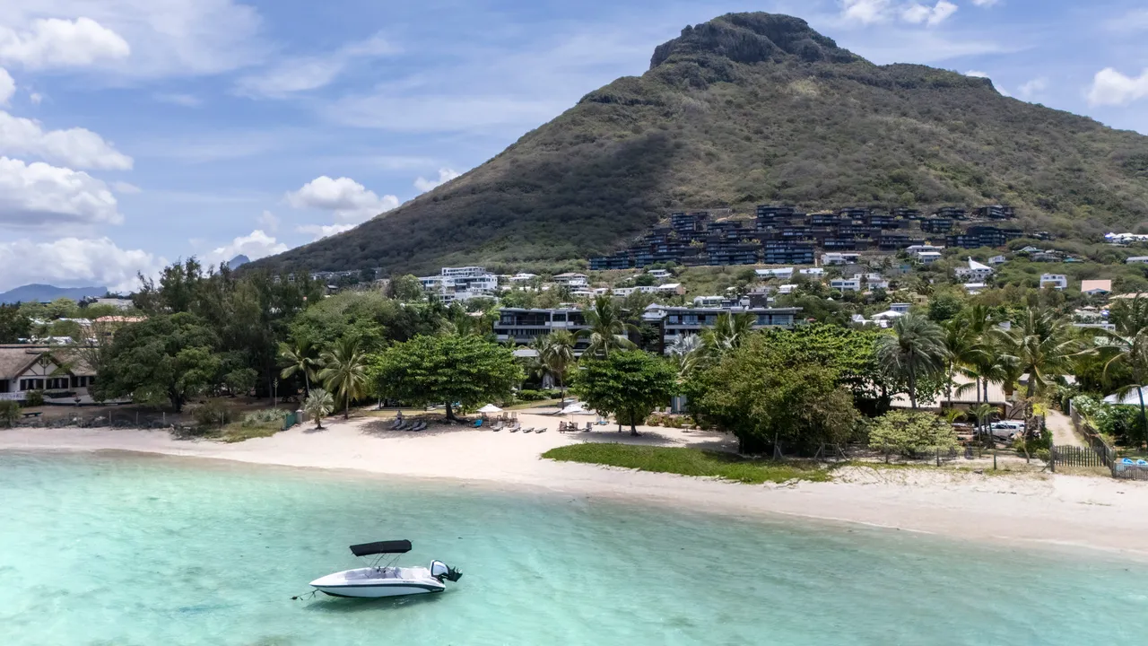 Plage de sable fin avec des eaux translucides et un accès direct à la mer.  
Végétation côtière ajoutant une touche naturelle à la promenade.  
Montagne en arrière-plan offrant un contraste avec le paysage côtier.  
Bateau à moteur amarré, apportant une touche maritime à l'ensemble.  
Espace dégagé permettant une vue imprenable sur l'oc