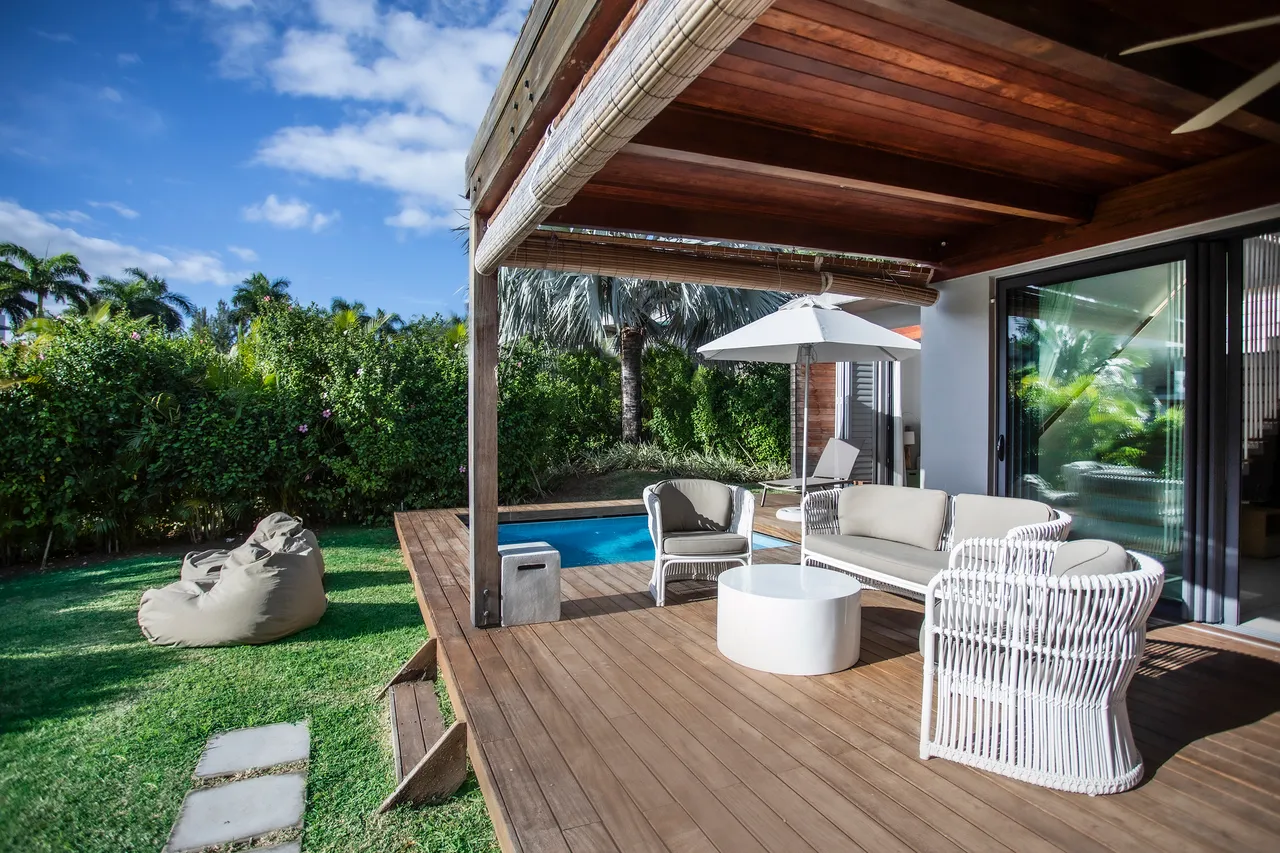 Terrasse avec mobilier en rotin et vue sur la piscine. Parasol et espace détente présent.