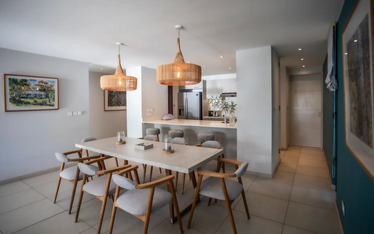 Salle à manger avec une grande table en pierre et chaises en bois. Éclairage suspendu en rotin ajoute de la chaleur.