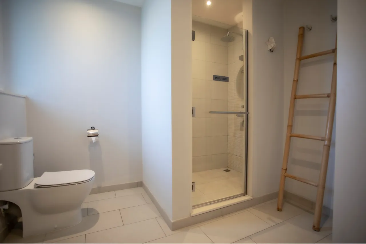 Salle de bain équipée d'une douche à l'italienne et de carrelage clair. Étagère en bois ajoutant une touche naturelle.
