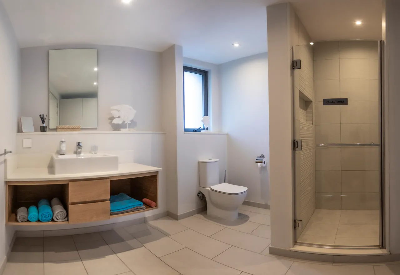 Salle de bain avec carrelage clair et douche à l'italienne. Rangements en bois sous le lavabo.