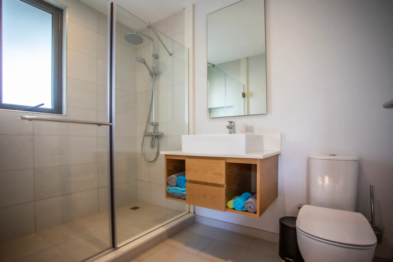 Salle de bain moderne avec douche à l'italienne et meubles en bois clair. Serviettes colorées soigneusement rangées dans le meuble sous vasque.