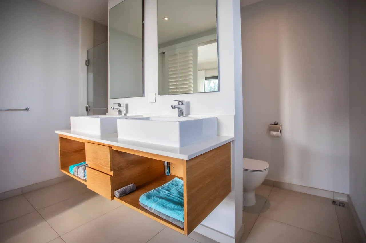 Salle de bain moderne avec double vasque et espace de rangement en bois. Éclairage naturel apporté par la fenêtre.