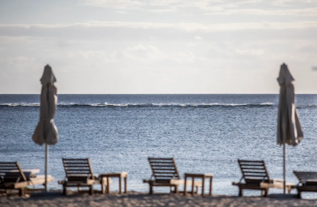Espace extérieur avec chaises longues en bois face à la mer. Parasols blancs pour l'ombre.