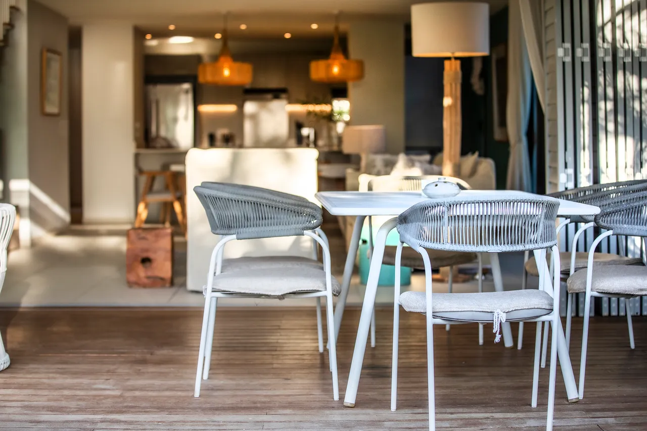 Mobilier en rotin et chaises ergonomiques sur terrasse en bois. Table blanche contemporaine.