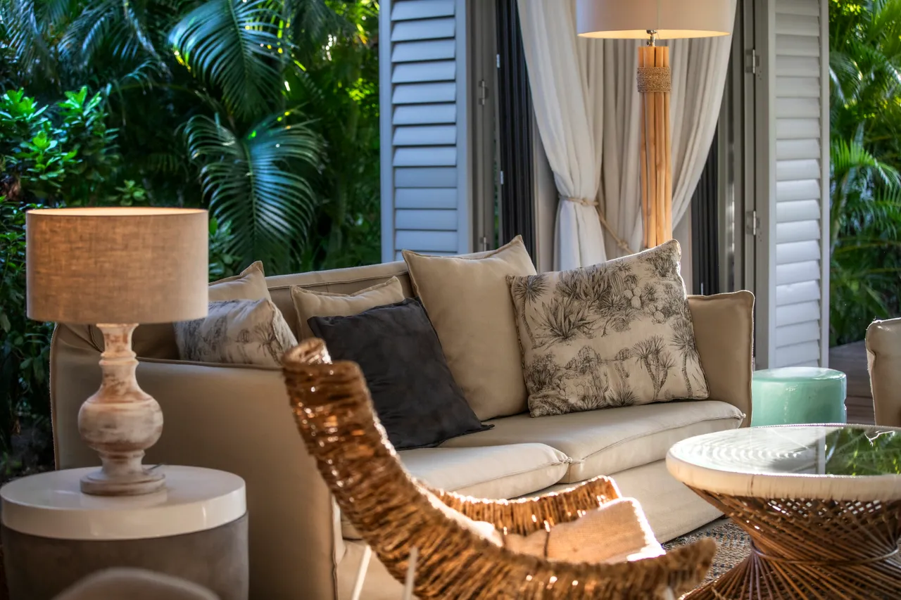 Salon avec canapé en cuir et coussins décoratifs. Lumière naturelle à travers les volets.