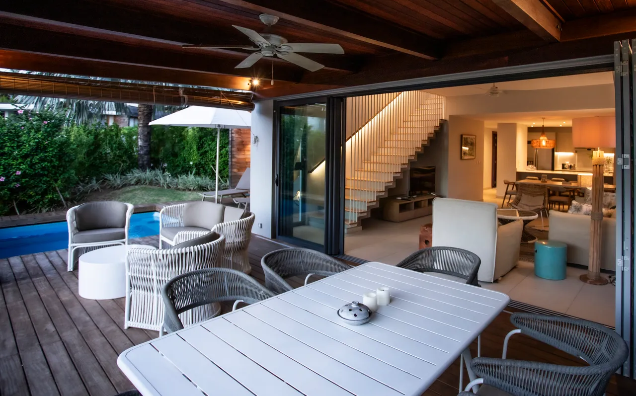Espace galerie avec mobilier en rotin et tables blanches. Ouverture sur le jardin et la piscine.