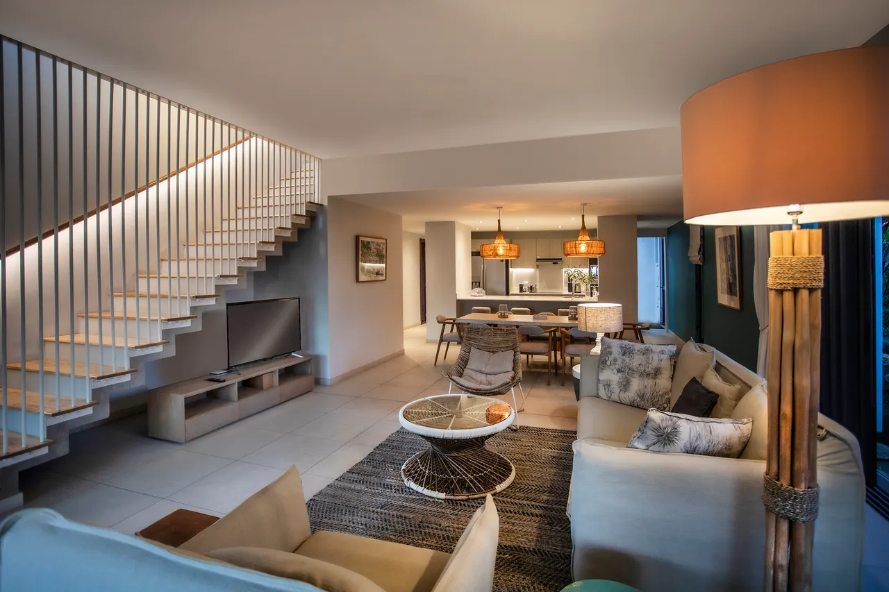 Espace salon avec un canapé confortable et une télévision. Éclairage chaleureux créé par des lampes suspendues.
