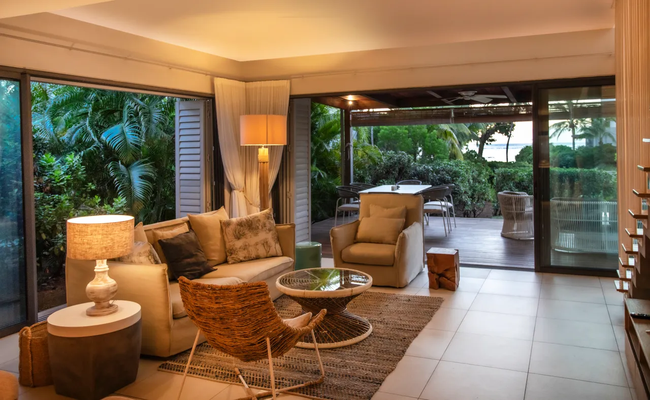 Espace galerie avec de grandes baies vitrées, ouvrant sur le jardin. Mobilier en rotin et éclairage doux créent une atmosphère détendue.
