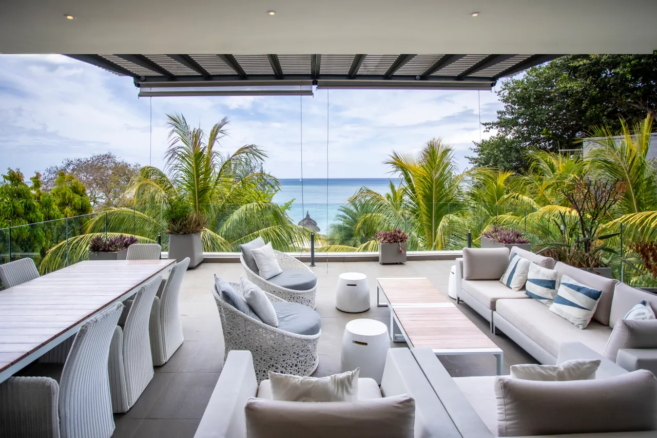 Teintes claires des meubles créent une atmosphère relaxante sur la terrasse. Une grande table à manger offre une vue sur la mer.