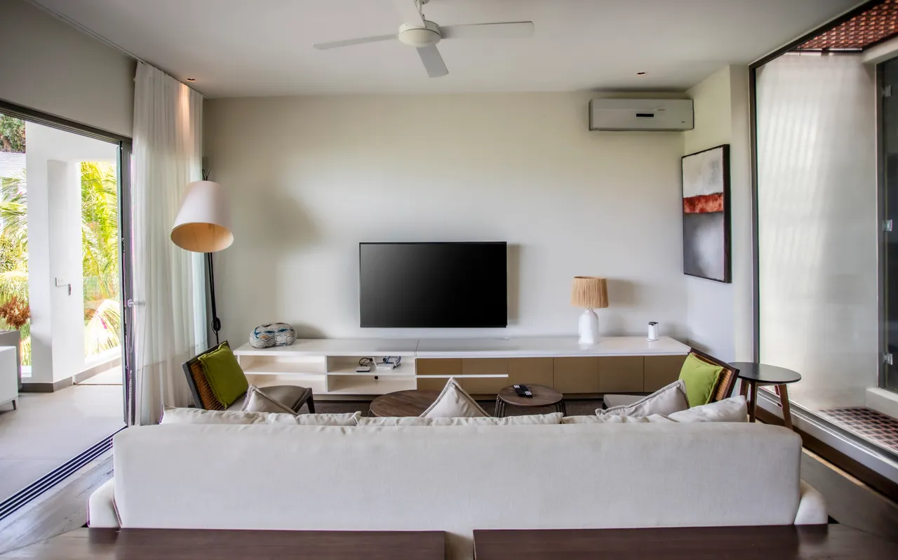 Teintes douces et mobilier moderne dans un salon lumineux. Télévision murale et accès direct à l'extérieur.