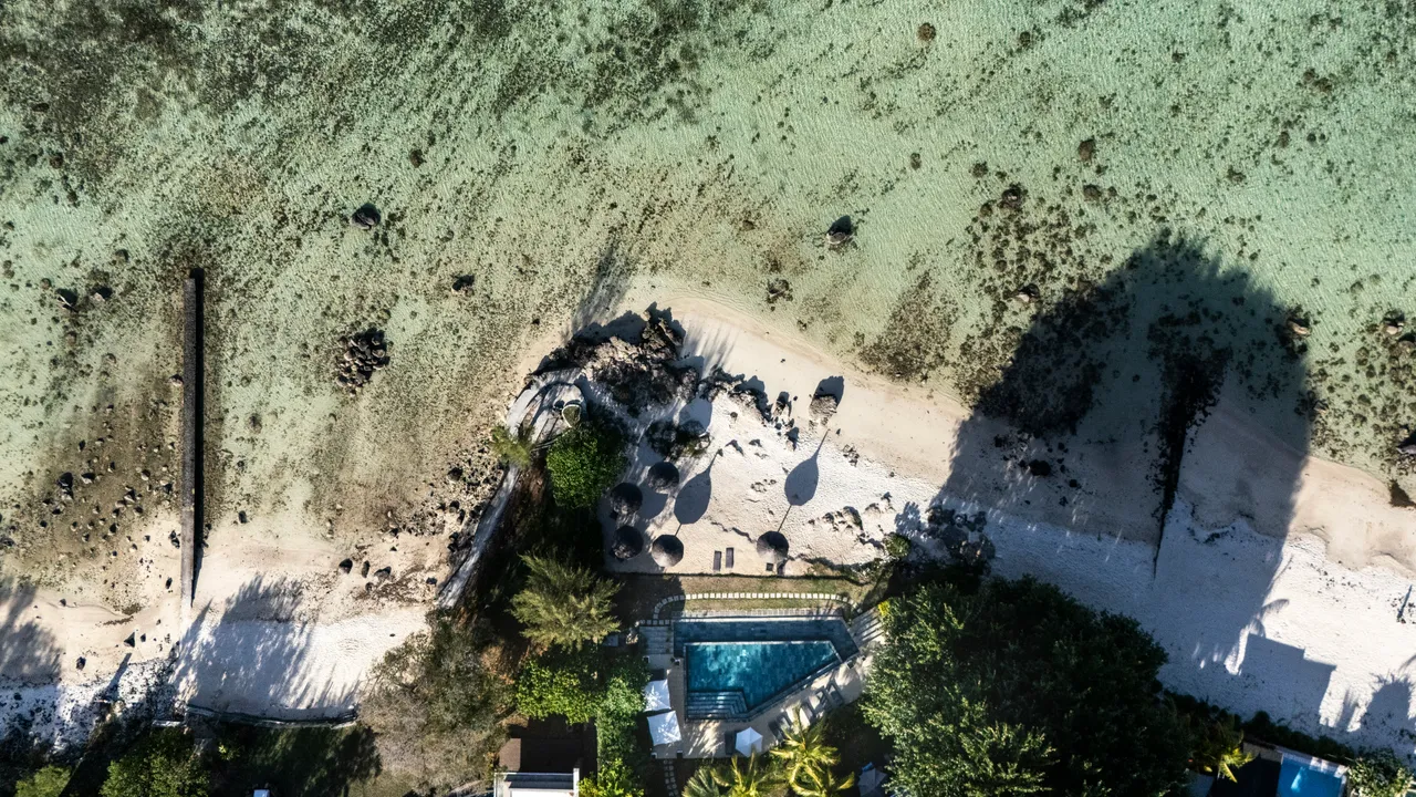 Vue aérienne du rivage avec chaises longues et piscine. Récif corallien visible à proximité.