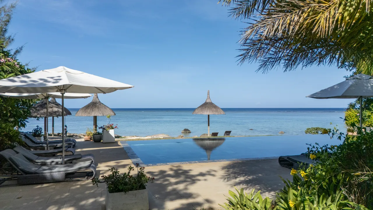 Espace extérieur avec piscine à débordement et parasols offrant une vue sur l'océan.
