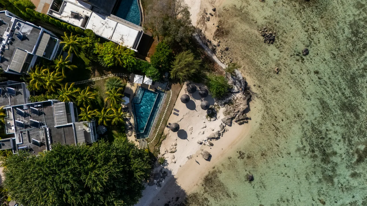 Espace extérieur avec chaises longues et parasols sur un sable clair. Vue sur l'eau.