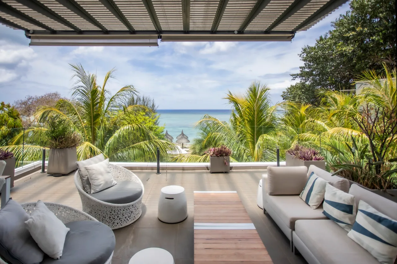 Mobilier en rotin et coussins aux teintes douces sur la terrasse. Vue dégagée sur la mer et les palmiers environnants.